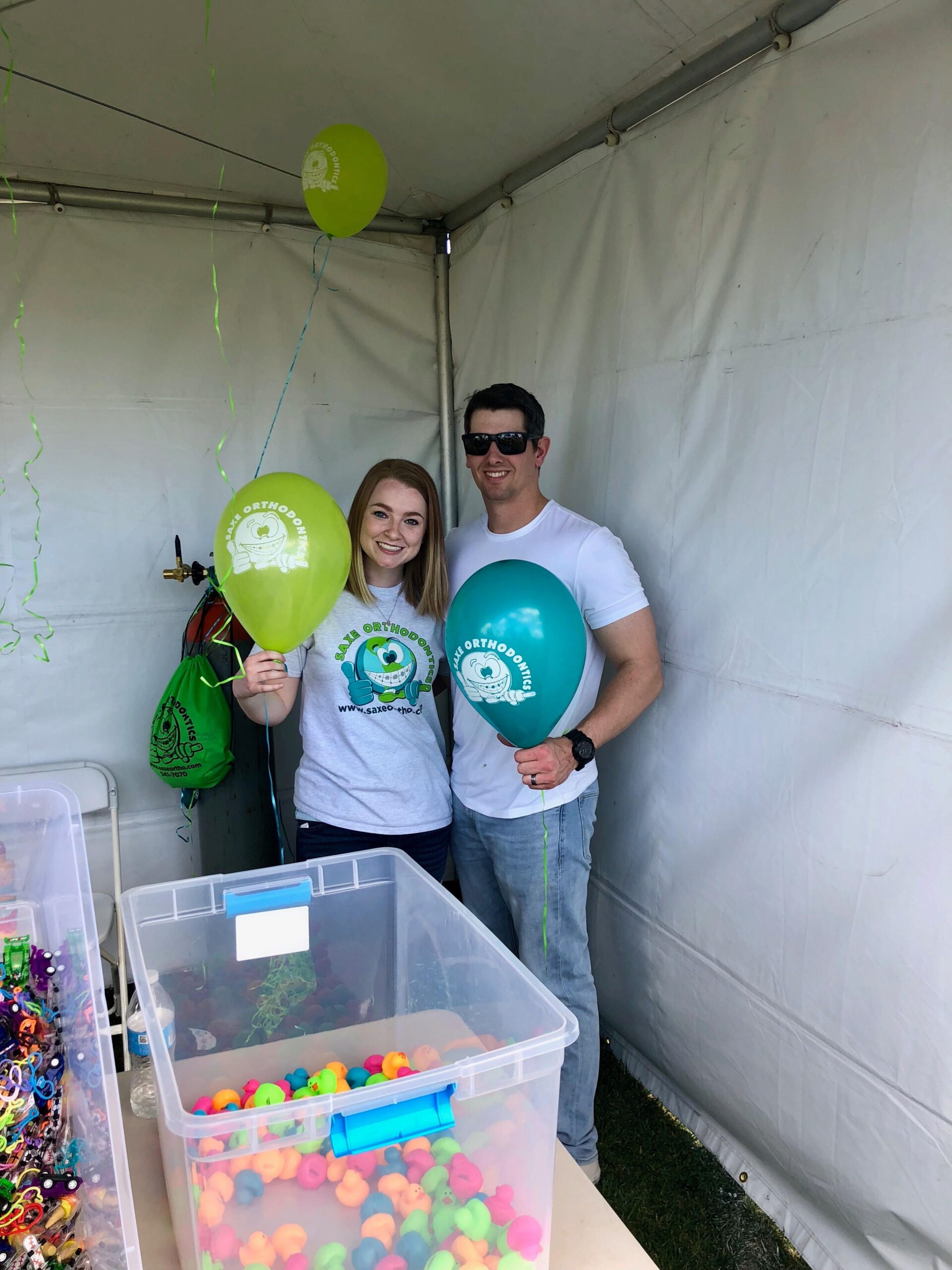 A couple posing for an event holding three balloons with the logo of Saxe Orthodontics.