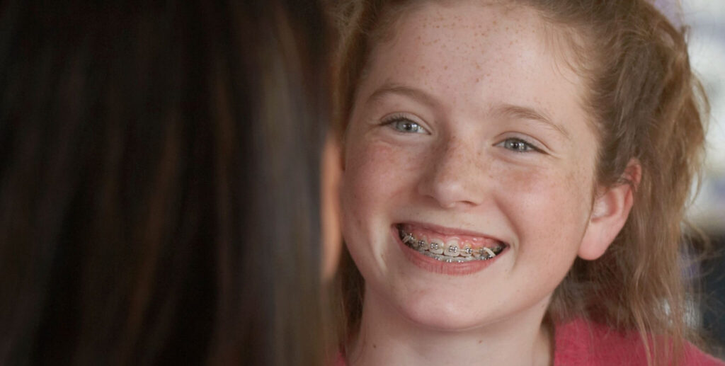 girl smiles showing off her braces for kids