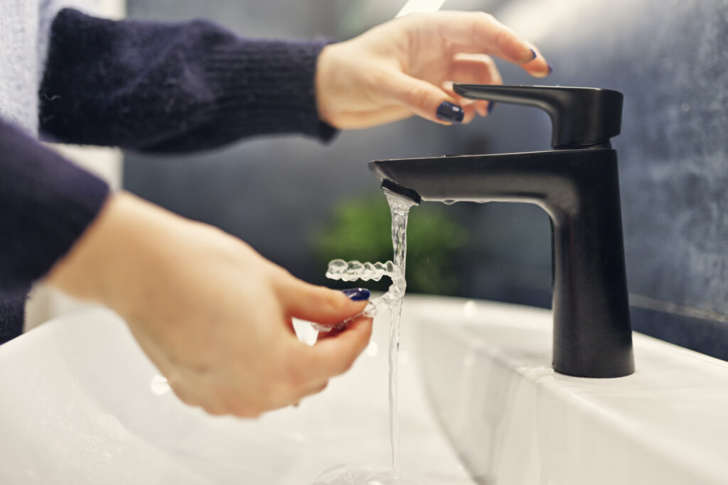Woman's hands cleaning clear retainer in sink, running under faucet, Saxe Orthodontics clean retainers