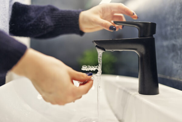 Woman's hands cleaning clear retainer in sink, running under faucet, Saxe Orthodontics clean retainers